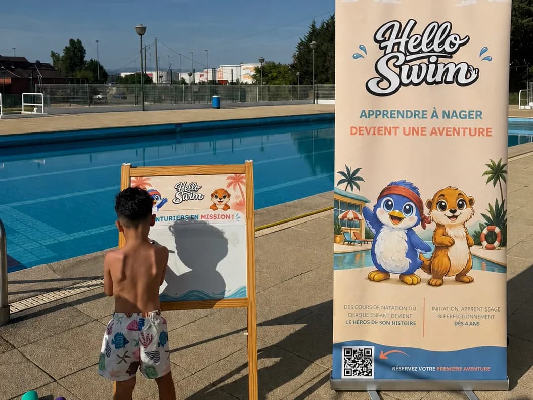Un enfant devant le tableau des aventuriers et le kakémono Hello Swim, au bord de la piscine
