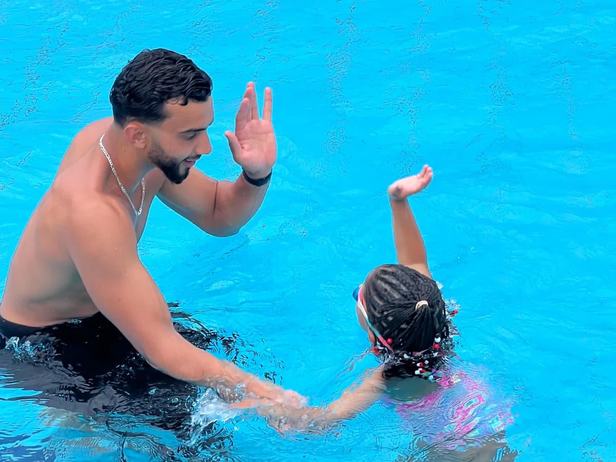 Un maître-nageur Hello Swim tape dans la main d’une petite nageuse, dans l’eau